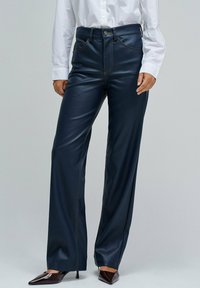 Pantalons amples en simili cuir navy avec des coutures tonales, une fermeture à bouton sur le devant et deux poches latérales. Associés à des talons aiguilles.