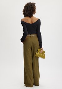Top negru off-shoulder din material ribbed, pantaloni largi cu talie înaltă în carouri verzi, accent cu lanț argintiu, ținând o geantă mică galbenă lucioasă.