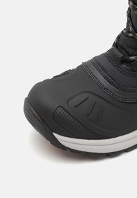 Botte étanche noire avec une coque de protection en caoutchouc texturé, une tige en mesh et une semelle intermédiaire blanche. Présente des lignes d'accent et un talon renforcé.