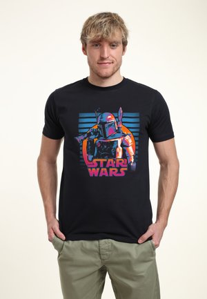 Camiseta negra con un gráfico colorido de un personaje en armadura, con el texto "STAR WARS" en negrita rosa debajo de un círculo naranja y rayas azules.