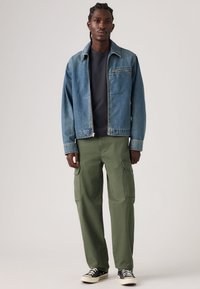 Τζιν μπουφάν σε ανοιχτό μπλε, συνδυασμένο με χακί cargo παντελόνια με πλαϊνές τσέπες. Μαύρα αθλητικά παπούτσια ολοκληρώνουν το σύνολο.