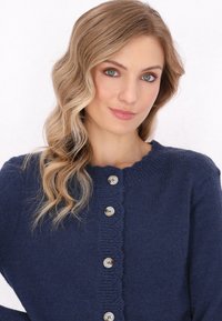 Navy blue knitted cardigan with a scalloped collar, featuring five circular buttons down the front. Soft texture, casual design.