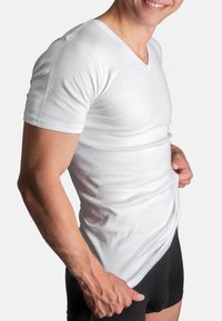 White short-sleeve V-neck t-shirt made of soft fabric, fitted design, and smooth texture, worn over black shorts.