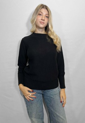 Maglione nero lavorato a maglia con collo rotondo e polsini a costine. Indossato con jeans in denim azzurri. Tessuto liscio, sagomatura aderente.