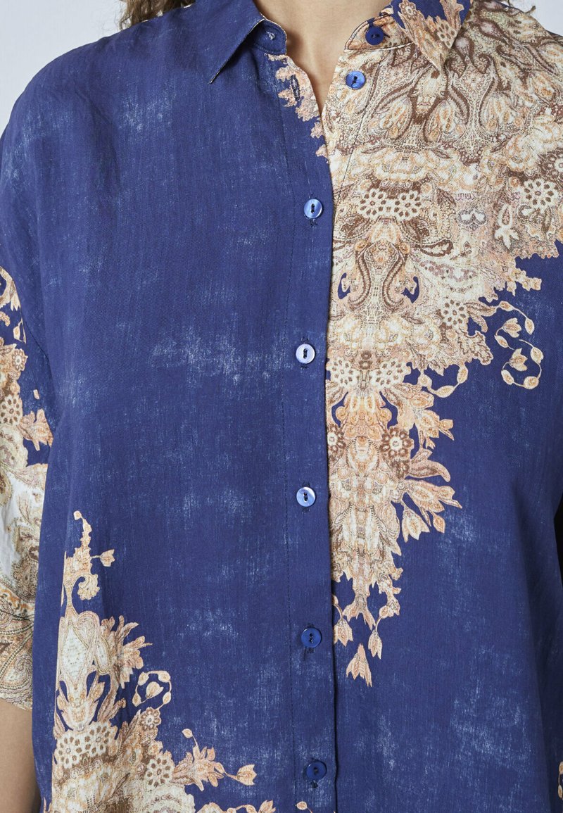 Blå skjorte med knaplukning, der har et struktureret paisley-mønster i beige og creme på den ene side. Letvægtsstof med en afslappet pasform.