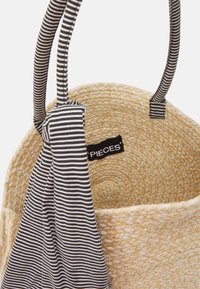 Borsa di paglia intrecciata con dettagli e manici in tessuto a righe bianche e nere. Etichetta interna visibile. Forma rotonda, texture naturale.