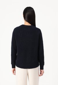 Navy blue knitted sweater with a round neckline, long sleeves, and a slightly curved hem. Made from a soft, textured fabric.