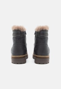Bottes de cheville en cuir noir avec une finition texturée et un doux bord en fourrure beige, dotées d'une semelle robuste marron et d'une fermeture éclair à l'arrière.
