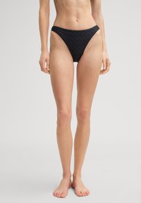 Schwarze Bikiniunterhose mit einem hoch geschnittenen Design, aus weichem Material mit einem dezenten Allover-Muster. Hohe Beinausschnitte und minimale Abdeckung.