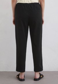 Zwarte katoenen broek met een elastische tailleband, rechte pijpen en zijzakken. Glad materiaal met een casual pasvorm.