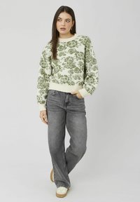 Pull en tricot avec motif floral vert sur fond crème, encolure ronde, poignets côtelés, associé à un jean gris taille haute et des baskets beige.