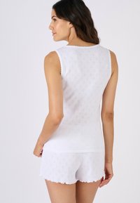 Canottiera bianca con bordi smerlati e pantaloncini abbinati, con un motivo a diamanti piccoli e testurizzati. Tessuto morbido, vestibilità casual.