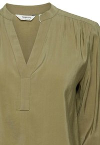 Blusa verde oliva realizzata in tessuto morbido, con scollatura a V, maniche arricciate e una cucitura centrale con dettagli di cucitura ben curati.