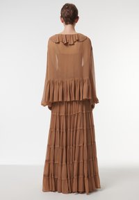 Robe longue en brown à plusieurs couches présentant un matériau transparent, un col froncé et un design en niveaux. La partie supérieure est ample avec de douces volants.