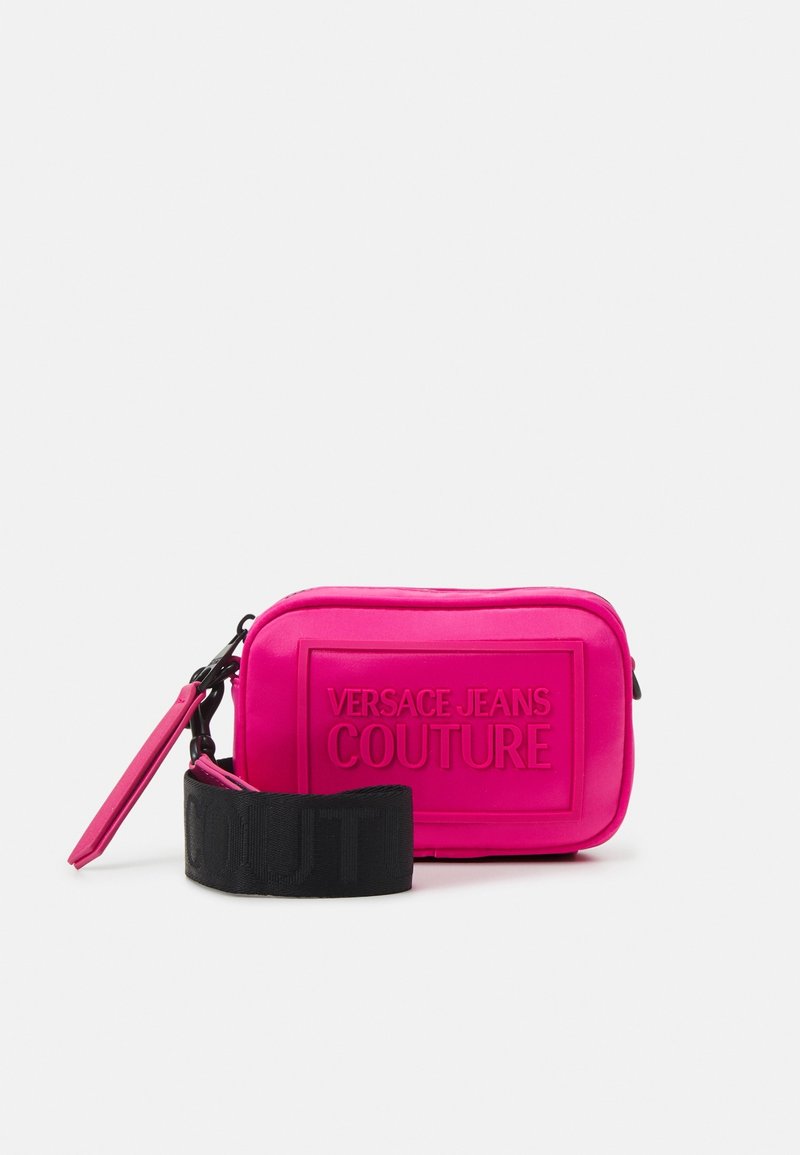 Pink Versace Jeans Couture bag with a rectangular shape, embossed logo, and a detachable black fabric strap featuring the word "COUTURE."