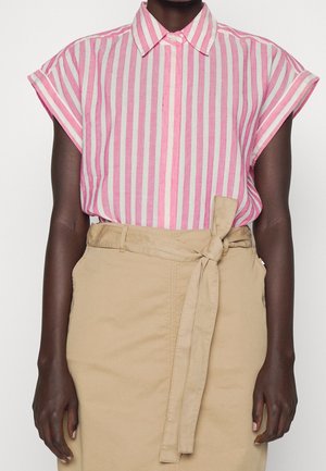 Persona vistiendo una camisa de manga corta con rayas verticales rosas y blancas, metida en una falda beige de cintura alta con cinturón anudado.