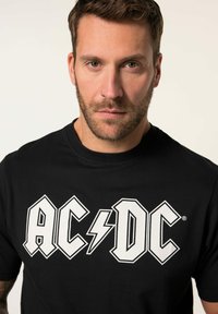 Zwarte katoenen t-shirt met het witte "AC/DC" logo met bliksemflits, ronde halslijn en korte mouwen, met een standaard pasvorm.
