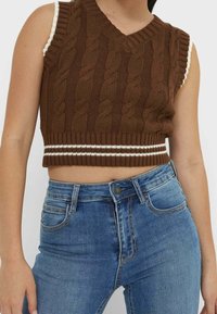 Hnědý crop top bez rukávů s kabelovým pletením a výstřihem do V, s bílými žebrovanými detaily na ramenou a jednobarevným žebrovaným spodním lemem.