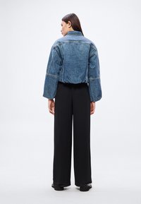 Farmerdzseki rövid szabással, bő ujjakkal és látható varrási részletekkel; fekete, bő szárú nadrággal párosítva.