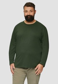 Donkergroene longsleeve t-shirt van zachte stof met een ronde halslijn. Gedeeltelijk gecombineerd met lichtgekleurde broek, die een relaxte pasvorm toont.