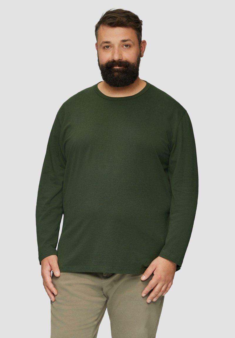 Donkergroene longsleeve t-shirt van zachte stof met een ronde halslijn. Gedeeltelijk gecombineerd met lichtgekleurde broek, die een relaxte pasvorm toont.