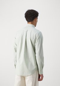 Light green long-sleeve shirt made of cotton with a collar, button details at the cuffs, and a curved hem. Features a back pleat for ease.