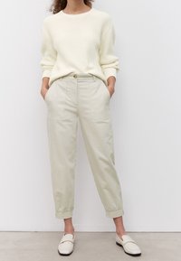 Krämfärgad stickad tröja med ribbat mönster, kombinerad med ljusbeige byxor med fickor. Vita slip-on skor fulländar outfiten.