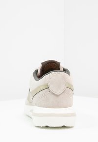 Vaaleanharmaat mokkanahkakengät, joissa on pyöreä muoto, kermavärinen pitoala ja vihreä korostuslinja. Sisältää vetokahvan kantapäässä.