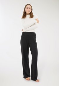Pantaloni neri a gamba larga con una texture morbida e vita elastica, abbinati a un dolcevita bianco a maniche lunghe aderente. Stile casual e confortevole.