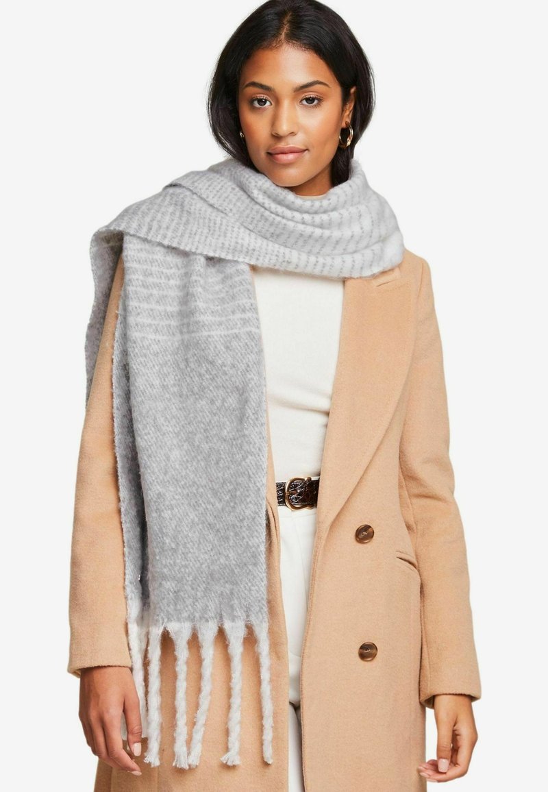 Grå tekstureret tørklæde med frynser, draperet over en beige frakke. Tørklædet har et subtilt mønster og blødt, varmt strikkemateriale.