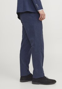 Pantaloni dintr-un amestec de in de culoare bleu marin, cu croială dreaptă, având o textură subtilă și asortați cu pantofi din suede negru.