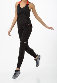 Musta toppi punaisilla olkaimilla ja mustat legginsit, joissa on tekstuuripaneelit, yhdistettynä harmaisiin urheilujalkineisiin. Nike-logo näkyy legginsissä.