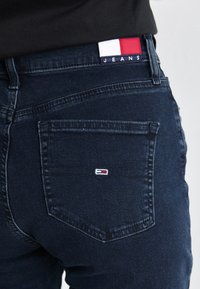 Dark blue denim jeans featuring a back pocket with a small logo, and a waistband label in red, white, and blue with the text "JEANS."