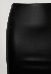 Svart läderkjol med en slät yta, hög midja och en stilren design. Stickningar synliga längs sömmen på sidan.