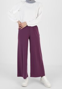 Paarse wijde broek gemaakt van zachte stof, met een elastische tailleband. Gecombineerd met een witte lange mouwen top en witte sneakers.