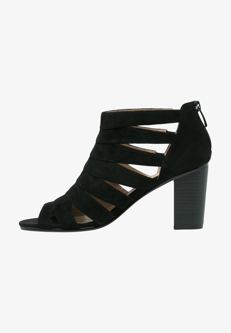 Sandale en daim noir avec plusieurs brides horizontales, design ouvert à l'avant et un gros talon carré. Fermeture zippée à l'arrière pour un enfilage facile.