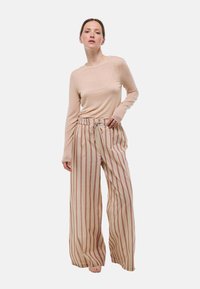 Haut beige à manches longues associé à un pantalon large avec des rayures verticales rouges et beiges, taille à cordon de serrage et texture de tissu douce.