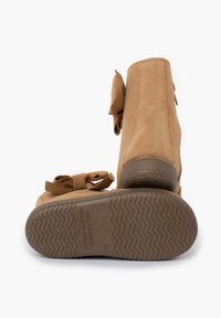 Botines de ante en tono arena con punta redondeada, adornados con un acento de lazo. La suela de goma presenta un patrón en zigzag para mayor tracción.