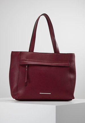 Sac cabas en cuir rouge foncé avec doubles bretelles, une poche zippée à l'avant avec tirette en cuir, et une petite plaque de marque argentée.