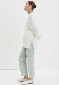 Fluffy witte sweater met zijsplitten, lichtblauwe rechte jeans en off-white flats, gepresenteerd tegen een eenvoudige achtergrond.