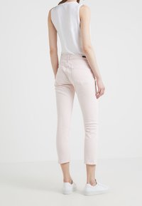 Pantalones de mezclilla rosas recortados con un diseño ajustado, que cuentan con dos bolsillos traseros y una cintura media. Combinados con zapatillas blancas.