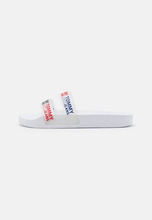 Sandale blanche à semelle plate avec deux brides transparentes, chacune arborant le logo "Tommy Jeans" en rouge, bleu marine et noir.