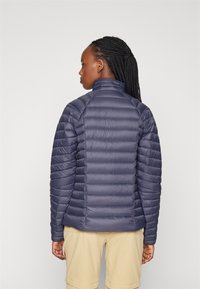 Jūrinės mėlynos puffer tipo striukė su horizontaliais siuvinėjimo raštais, aukštu apykakle ir sklandžia, blizgia tekstūra. Yra prigludusi, lengvo svorio.