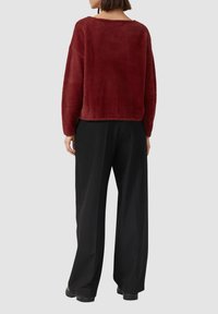 Maglione fuzzie color marocchino con vestibilità ampia, scollatura larga e maniche lunghe, abbinato a pantaloni neri a gamba larga con vita alta.