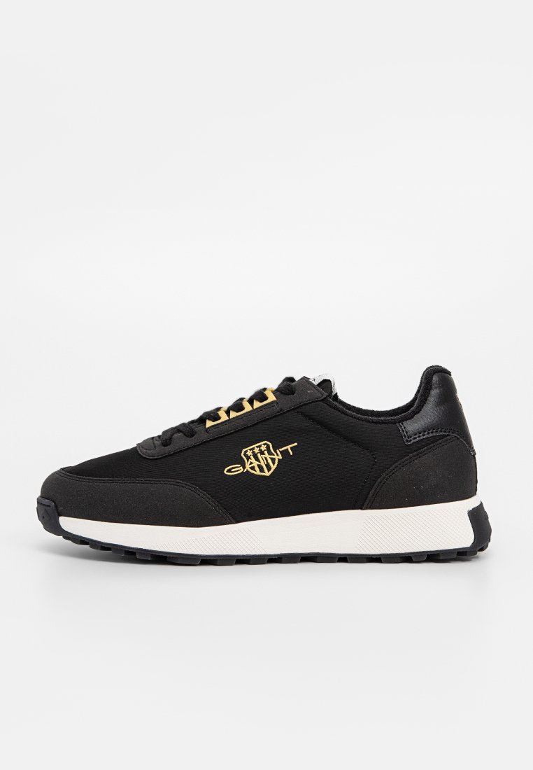 Svart sneaker i tyg med läderdetaljer, med en vit sula, guldlogotyp och svarta snören. Atletisk design med en strukturerad yta.