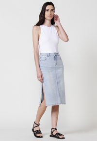 Svetlo modra denim krila s stranskimi razpoki, kombinirana z belo brezrokavno majico. Krilo ima klasičen kroj in temne kovinske dodatke.