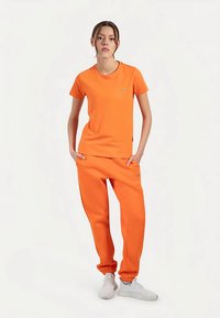 Orange cotton t-shirt and matching joggers with elastic cuffs. Features a small logo on the chest and side of pants. White sneakers worn.
