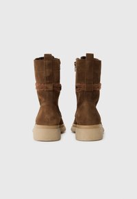 Brown suede ankle boots featuring a soft texture, short zip, and a band of brown wool around the shaft. Thick cream-colored rubber soles.