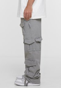 Pantaloni cargo gri cu multiple buzunare, croială relaxată și manșete ajustabile, asortați cu adidași albi. Material din amestec de bumbac.