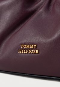 Bordinė odinė rankinė su auksiniu "TOMMY HILFIGER" logotipu. Medžiaga turi tekstūruotą paviršių ir susiraukšlėjimą viršuje.